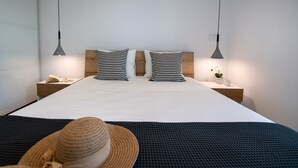 A neatly made bed with a white sheet and two patterned pillows, a wooden headboard, bedside lamps, a small bedside table with a book and glasses, and a hat on the bed. - High-end Luxury Apartment & Convenient Location (Tsoukalades)