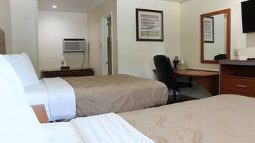 A hotel room with two beds, a desk, a chair, a mirror, and a wall-mounted TV.