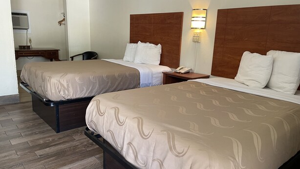 Une chambre d’hôtel avec deux lits, un bureau, une chaise et une table de chevet avec un téléphone et une lampe.