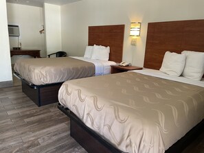 Habitación de hotel con dos camas, un escritorio, una silla y una mesita de noche con teléfono y lámpara.