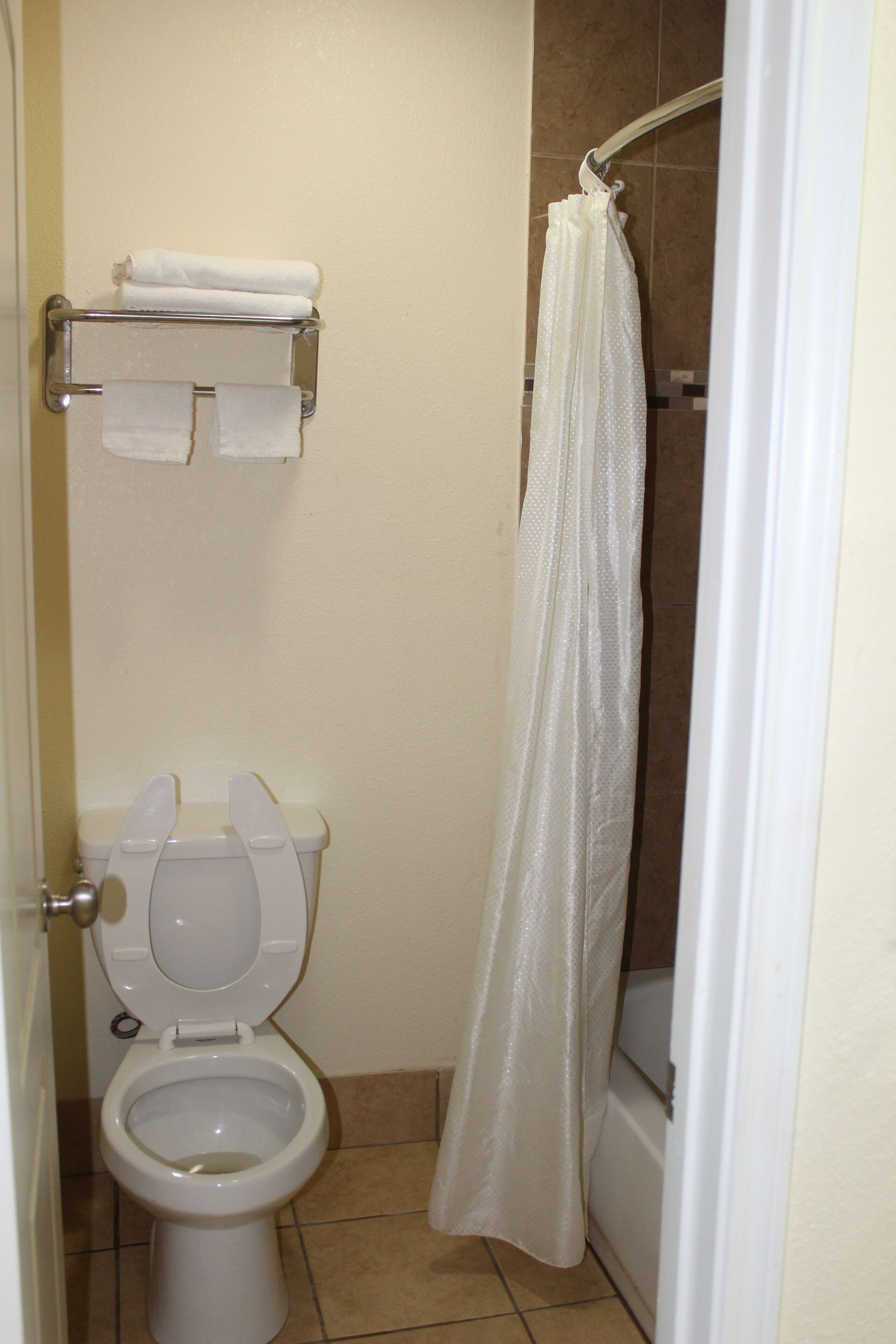 A bathroom with a toilet, a towel rack with folded towels, and a shower curtain.