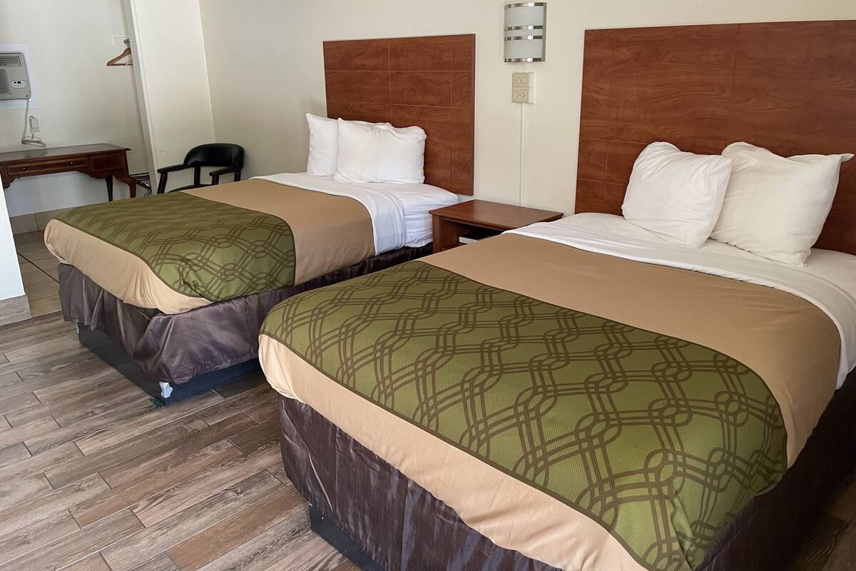 Two double beds with wooden headboards, a desk, and a chair in a hotel room.