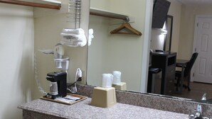 Une salle de bain d’hôtel dotée d’un comptoir en granit, d’une machine à café, d’un distributeur de serviettes et d’un miroir qui reflète un bureau et une chaise.