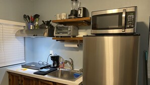 Una cocina con un refrigerador de acero inoxidable, un microondas, una cafetera y un tostador sobre una repisa de madera.