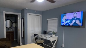 Un dormitorio con cama, escritorio, silla, televisión y puerta.