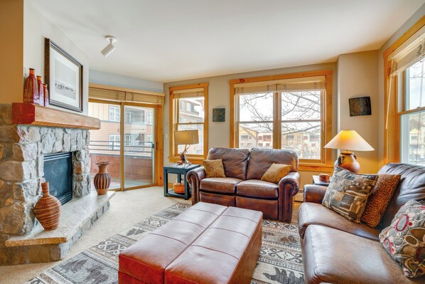 A cozy living room with a stone fireplace, leather sofas, and a large window with a view of the city. - Ski-In/Out Condo w/ Hot Tub Access in Keystone! (Keystone)