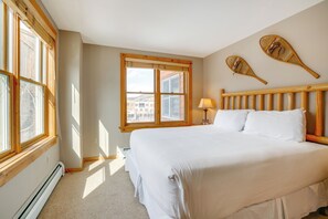 A bedroom with a large bed, wooden headboard, two windows with blinds, a lamp, and two wall-mounted paddleboards. - Ski-In/Out Condo w/ Hot Tub Access in Keystone! (Keystone)