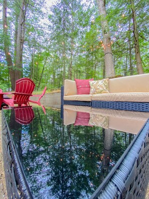 A serene outdoor seating area with a reflective water surface, surrounded by trees and string lights. - Rustic Log Cabin - Walking Distance to Village! (Lake George)