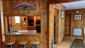 Ett rustikt kök med träväggar, en bardisk med barstolar och en skylt som visar texten ”Adirondacks 1892”.