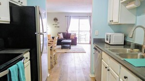 A kitchen with a black refrigerator, white cabinets, a microwave, and a sink. There is a wooden dining table with chairs and a sofa in the background. - Cliffside Cottage 3 - Updated - Near Silver Dollar (Branson)