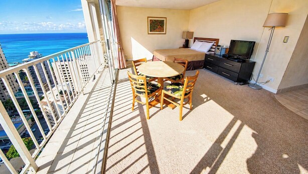 A balcony with a table and chairs, a bed, a television, and a ceiling fan.