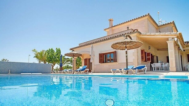 A poolside view of a house with a swimming pool, lounge chairs, and umbrellas.
