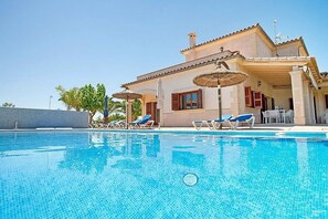 Vista da piscina de uma casa, com espreguiçadeiras e guarda-sóis.