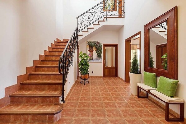Uma escadaria com corrimão de ferro forjado, um banco com almofadas verdes e um espelho grande na parede.