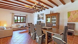 A dining area with a wooden table and wicker chairs, a sofa, and a cabinet with glass doors.
