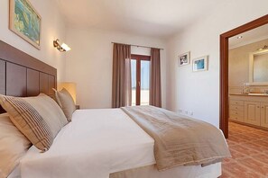 A hotel room with a bed, a nightstand, a lamp, a window with curtains, and a bathroom visible through an open door.