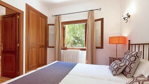 A bedroom with a large bed, wooden wardrobe, a window with curtains, a bedside lamp, and patterned pillows.