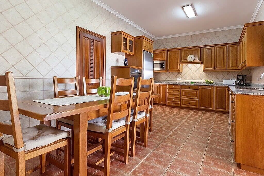 A kitchen with wooden cabinets, a dining table with chairs, and a tiled floor.