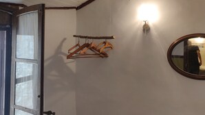Een kamer met een houten plafond, een wandspiegel, een houten dressoir en een kledingrek met hangers.