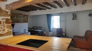 Een landelijke keuken met een houten werkblad en rode kastjes, een eethoek met stoelen, en een woonkamer met een bank.