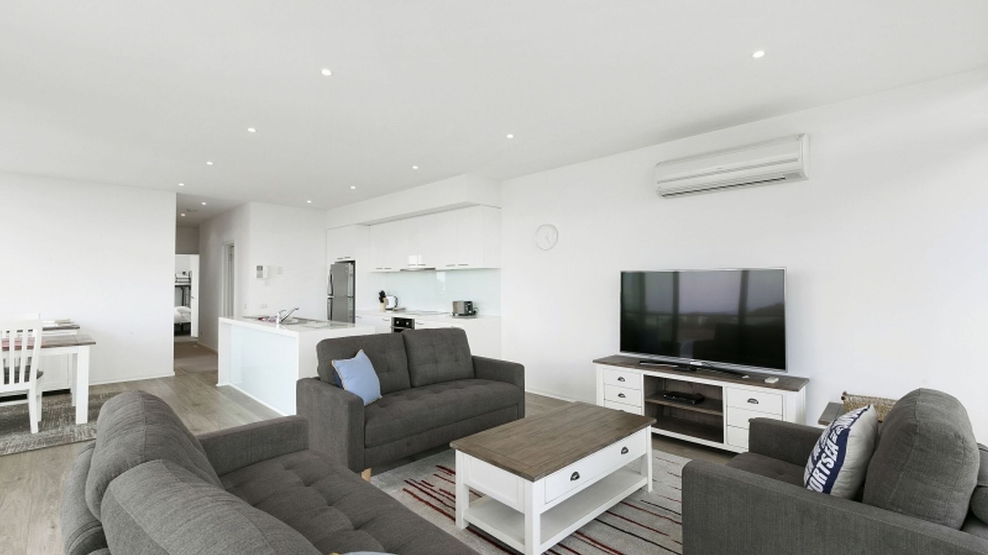 Uma sala de estar moderna com um sofá cinzento, uma mesa de centro e uma televisão de tela plana.