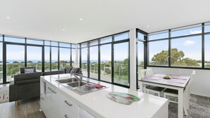 A modern kitchen with large windows, a dining area, and a view of the landscape. - Whitewater Apartment 201 Ocean Views Walk to Beach (TORQUAY)