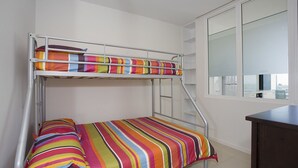 Un lit superposé avec une literie rayée aux couleurs vives, une fenêtre offrant une belle vue et un petit espace bureau.