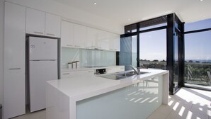 Une cuisine moderne avec des meubles blancs, un réfrigérateur encastré et une grande fenêtre donnant sur l’extérieur.