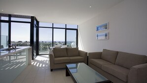 Un salon moderne avec un canapé, une table basse en verre et un coin repas offrant une vue sur la mer.