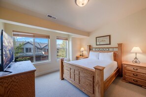 Une chambre à coucher avec un lit en bois, des tables de chevet, un bureau et une grande fenêtre.