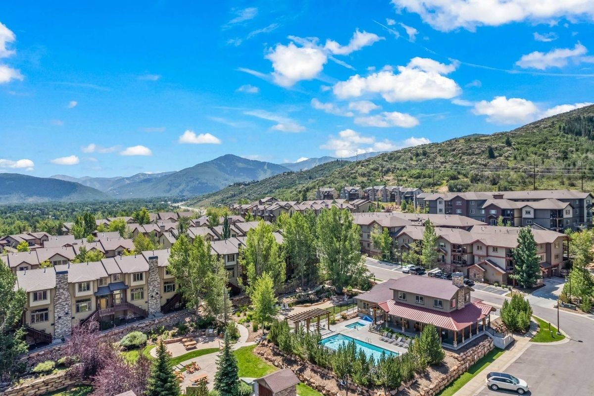 A residential complex with multiple apartment buildings, a swimming pool, and a mountainous backdrop.