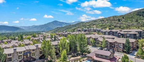 A residential complex with multiple apartment buildings, a swimming pool, and a mountainous backdrop.