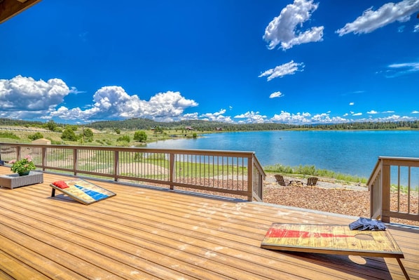 A wooden deck with lounge chairs overlooking a lake, surrounded by a wooden fence and a view of a forested landscape.
