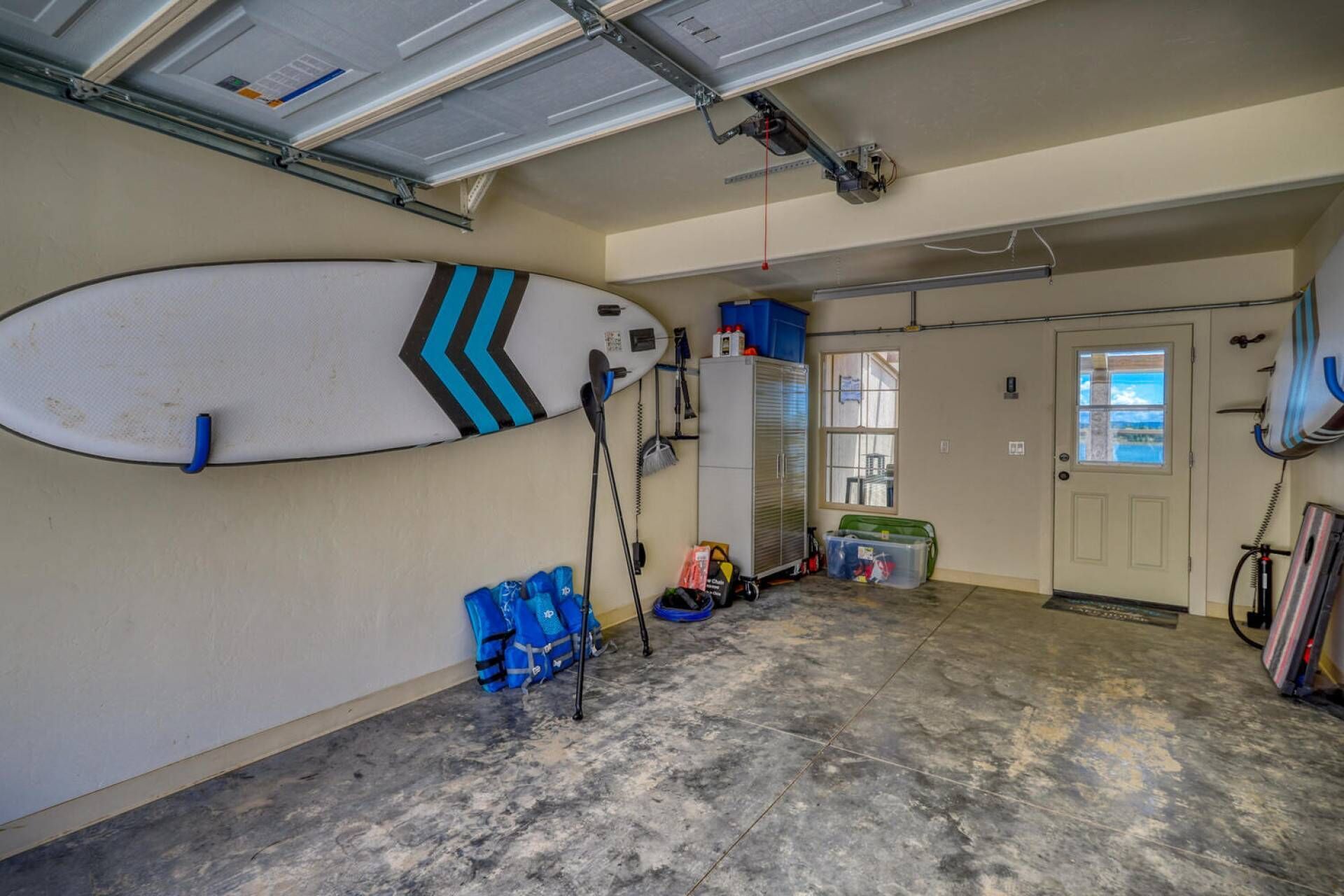 Un garage avec une planche de surf accrochée au mur, une porte donnant sur un beau paysage et divers objets éparpillés sur le sol.