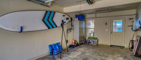 Un garage avec une planche de surf accrochée au mur, une porte donnant sur un beau paysage et divers objets éparpillés sur le sol.