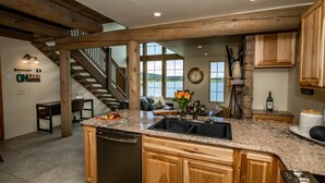 A spacious kitchen with granite countertops, wooden cabinets, and a built-in dishwasher. A large window offers a view of a lake.