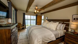 A bedroom with a large bed, wooden headboard, a ceiling fan, a view of a lake, and a wooden dresser.
