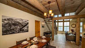 A dining area with a wooden table set for four, a chandelier, and a mountain landscape painting on the wall.