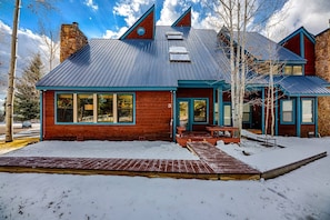 Une cabane avec une cheminée en pierre, un toit en métal et une terrasse en bois.