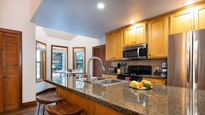 Cocina moderna con encimeras de granito, electrodomésticos de acero inoxidable, armarios de madera y una barra de desayunos con taburetes.
