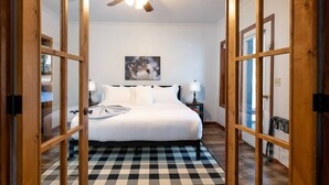 Un dormitorio con piso a cuadros, una cama con sábanas blancas, un ventilador de techo y un cuadro de un lobo en la pared.
