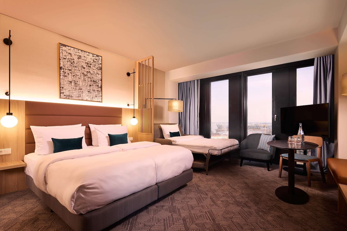 Ein Hotelzimmer mit einem großen Bett, einem Schreibtisch, einem Stuhl, einem Fernseher und einem Fenster mit Vorhängen.