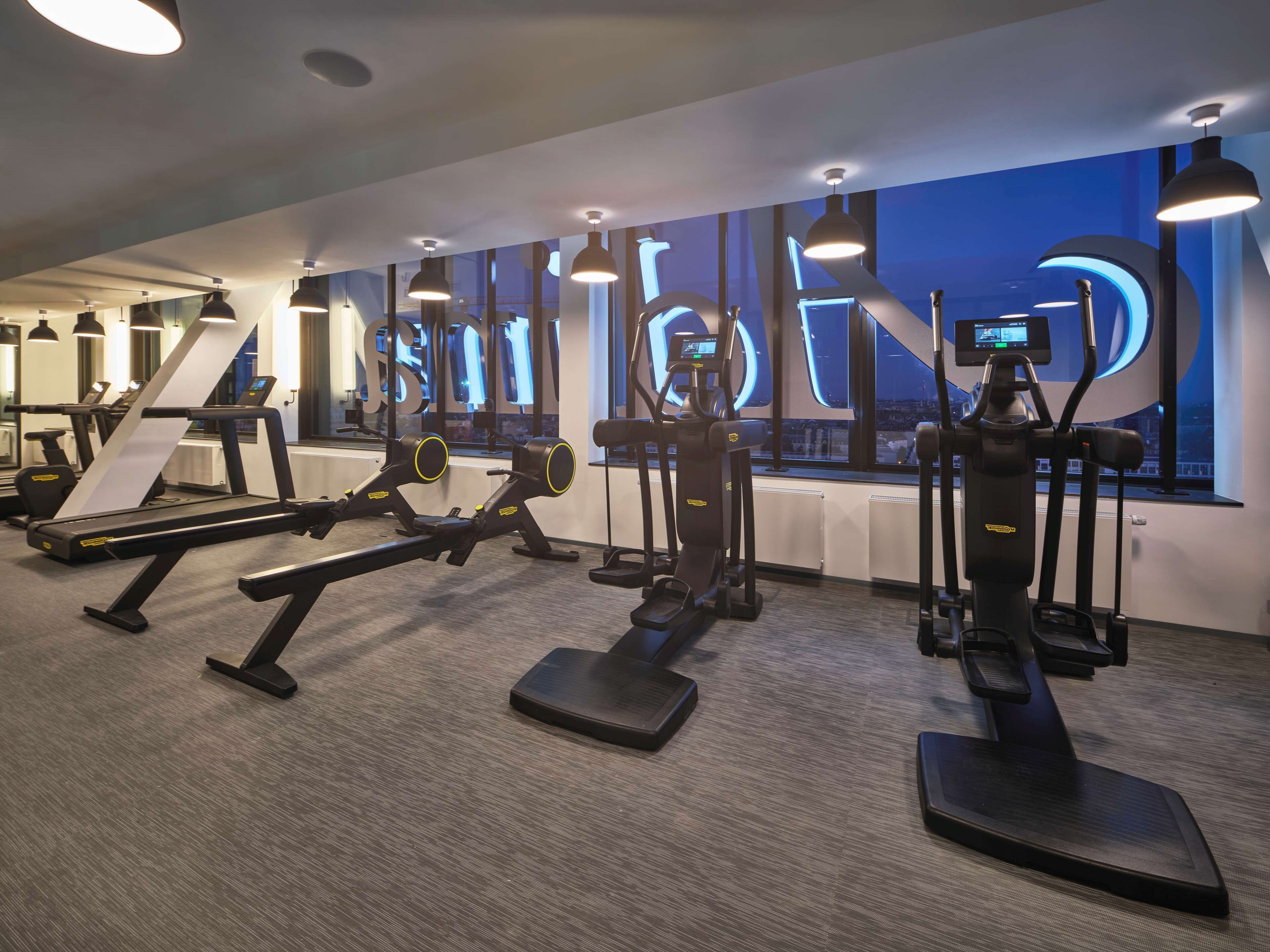 Un gimnasio moderno con diverso equipamiento de ejercicio, ventanas amplias y vistas a la ciudad.