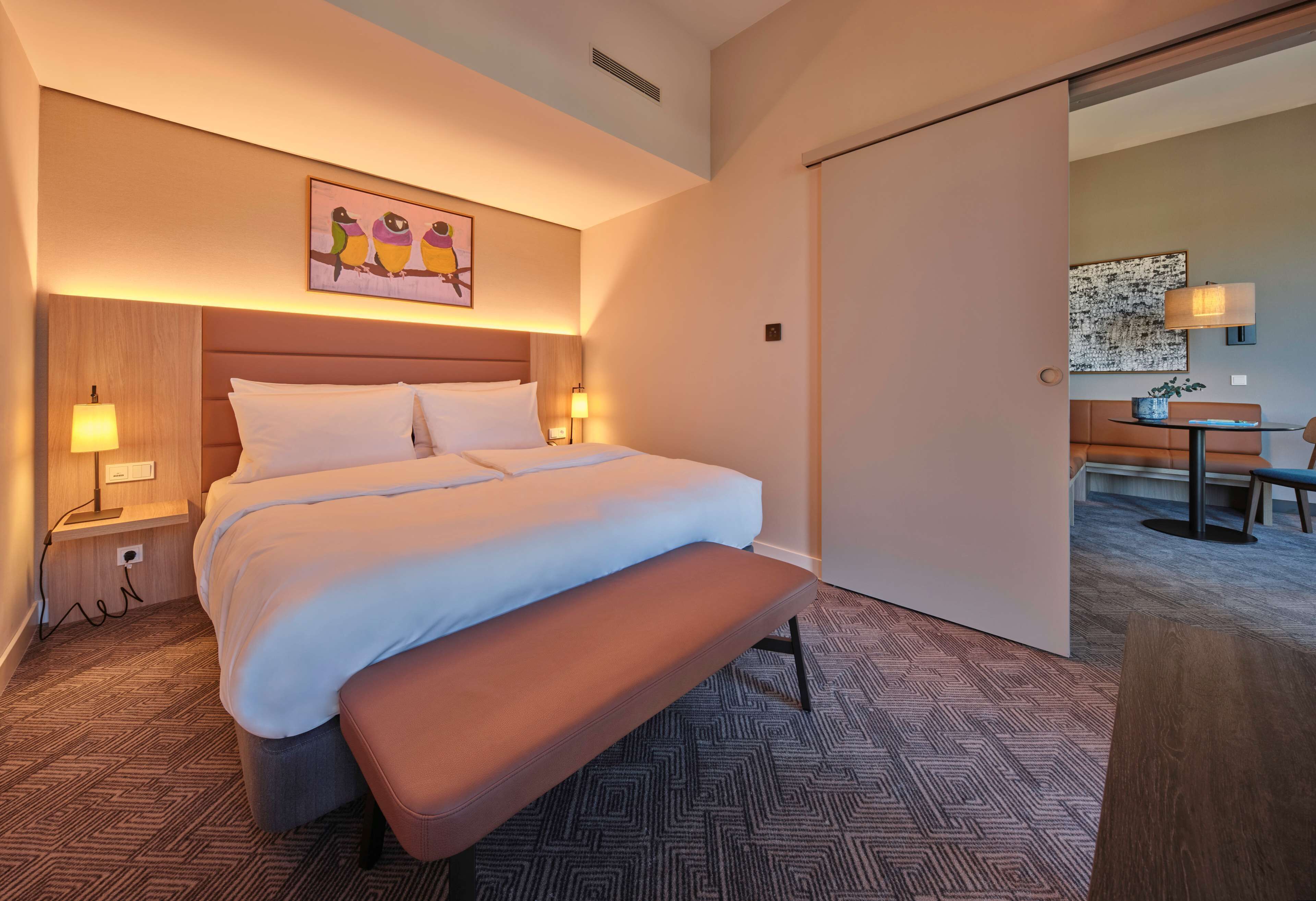 Une chambre d’hôtel avec un grand lit, une banquette, un bureau et une chaise.