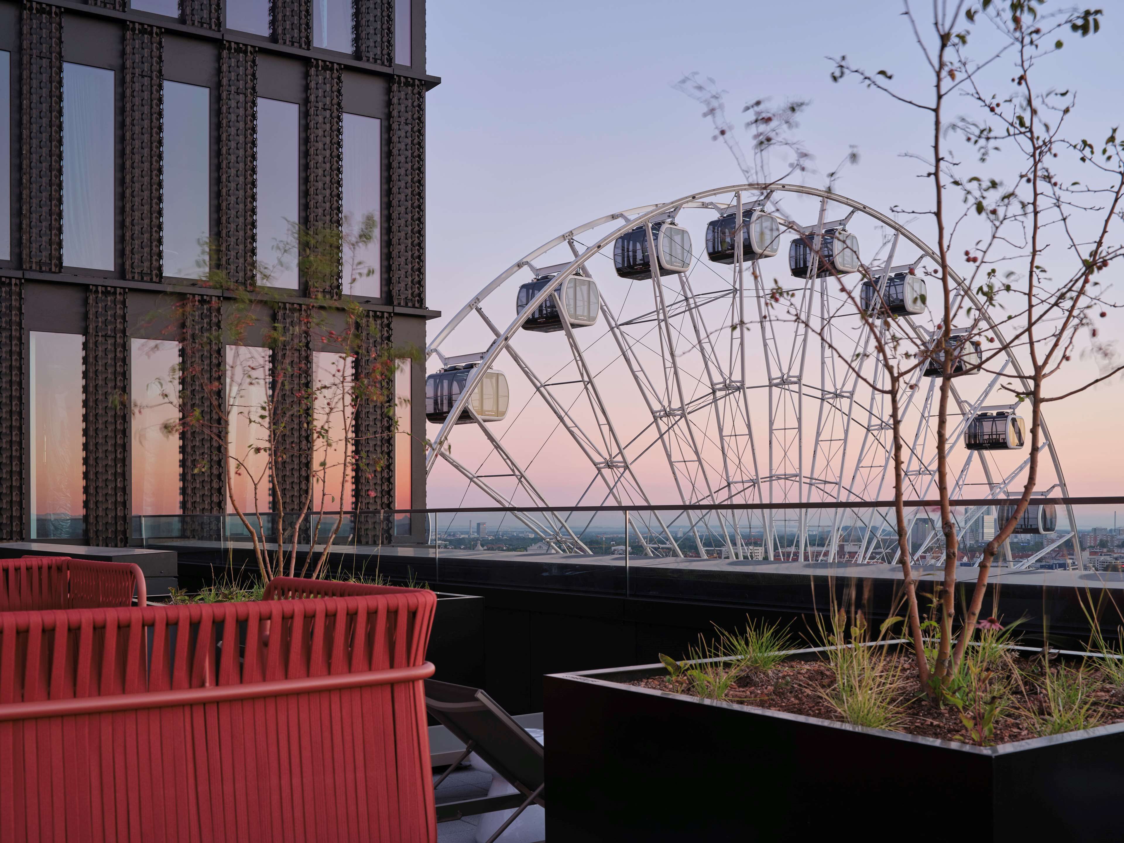 A modern building with a large Ferris wheel in the background, a glass railing, and a planter with plants.
