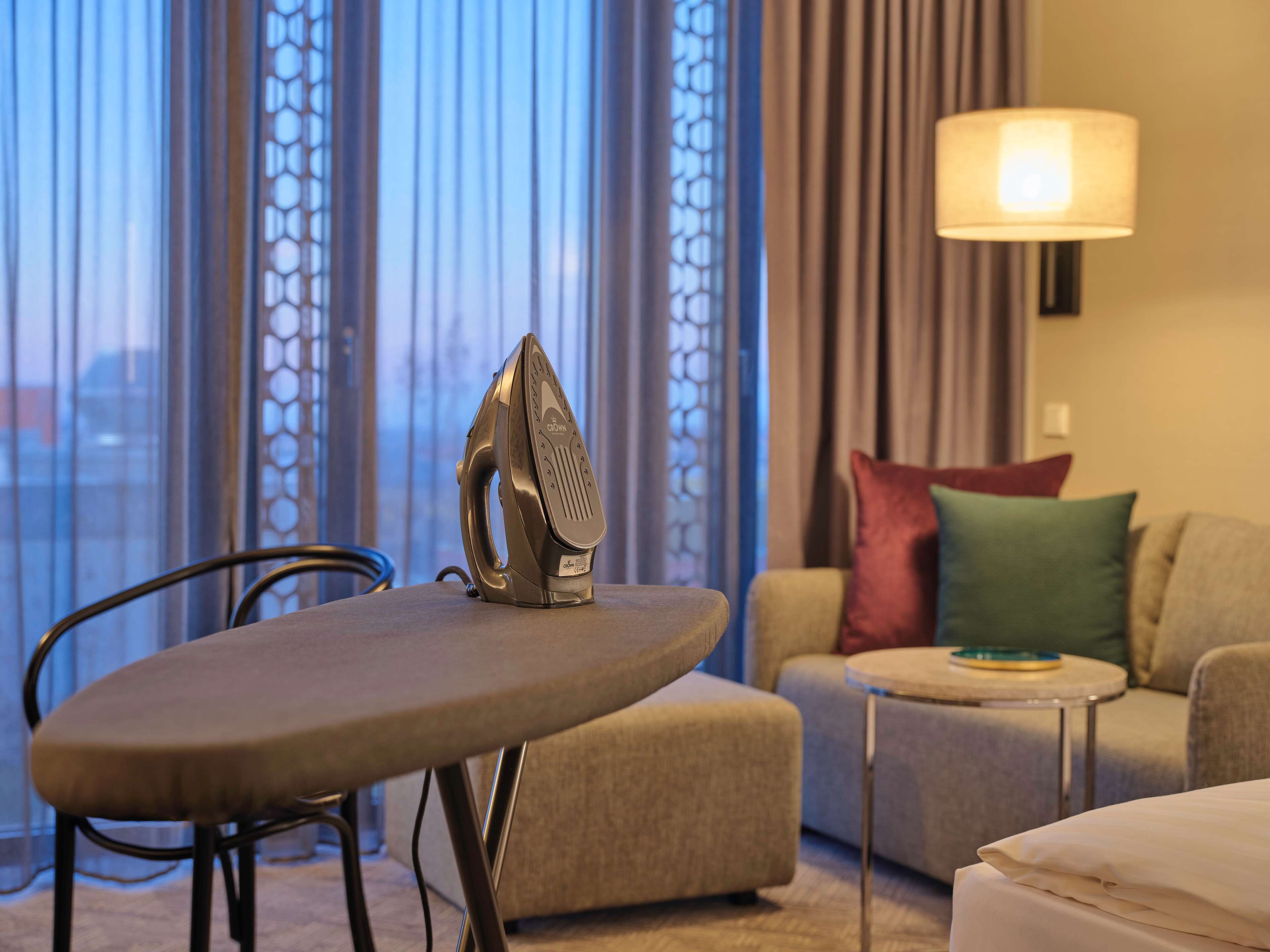 Ein Hotelzimmer mit Bügelbrett, einer Couch, einem kleinen Tisch und einer Lampe.