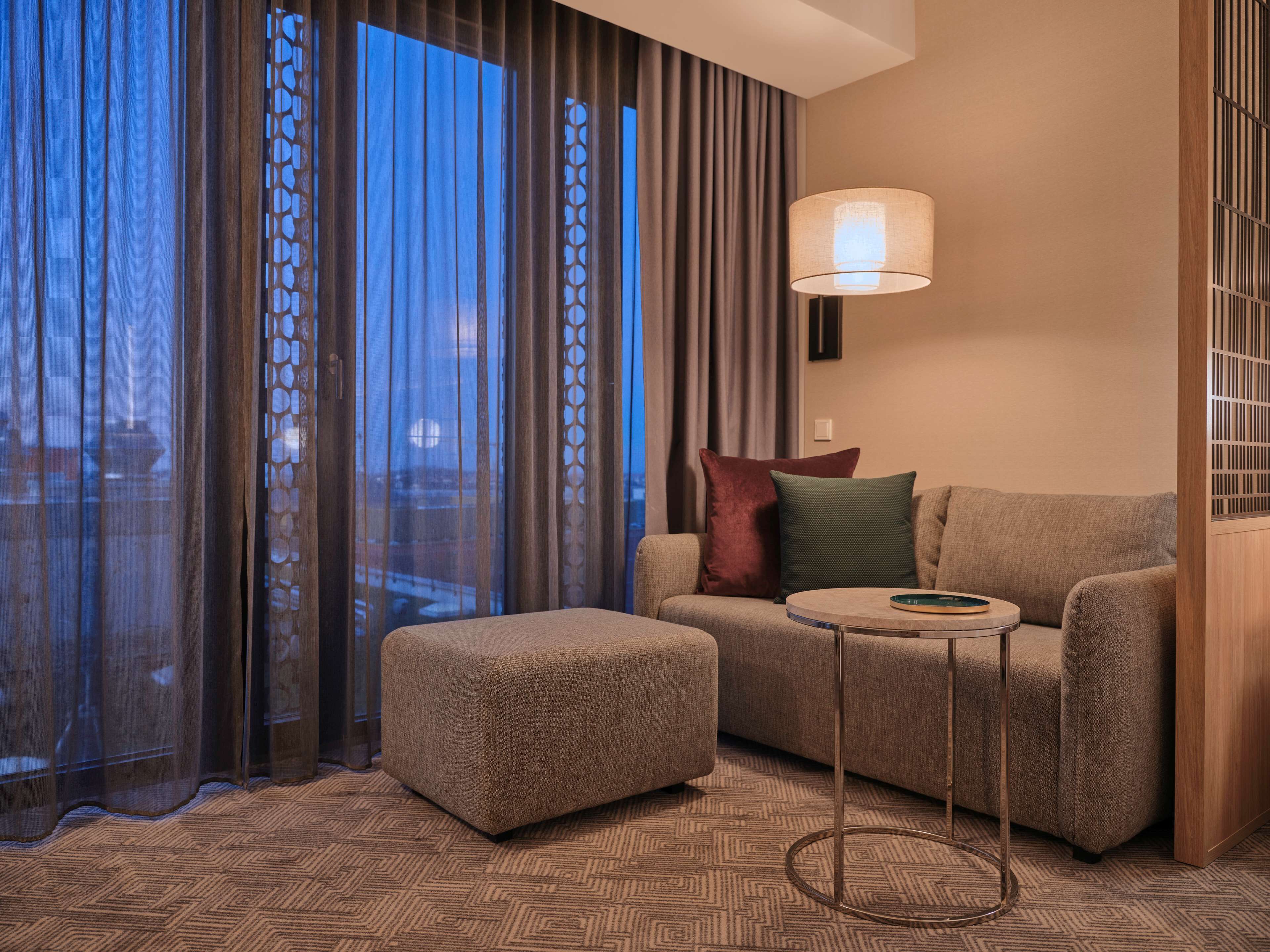 A modern living room with a sofa, ottoman, and a floor lamp.