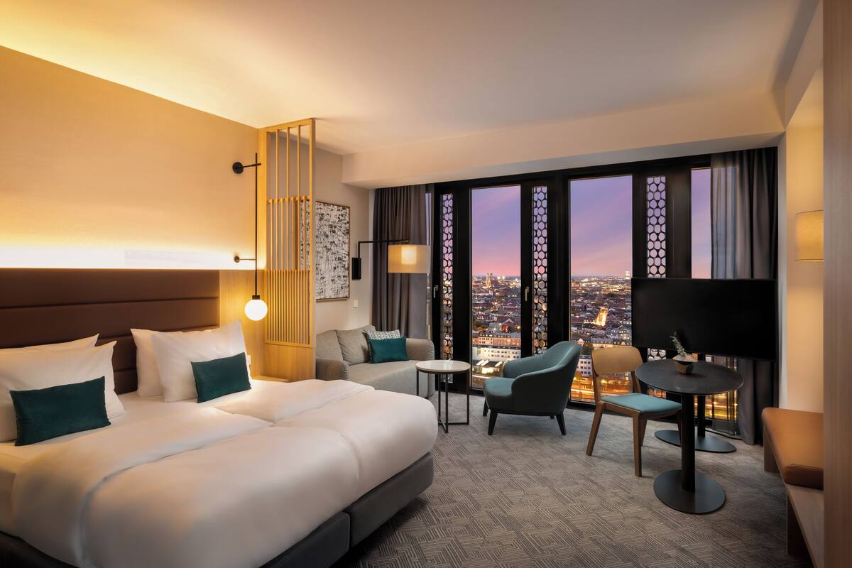 Ein Hotelzimmer mit Bett, Sofa, Fernseher und Blick auf die Stadtlandschaft.