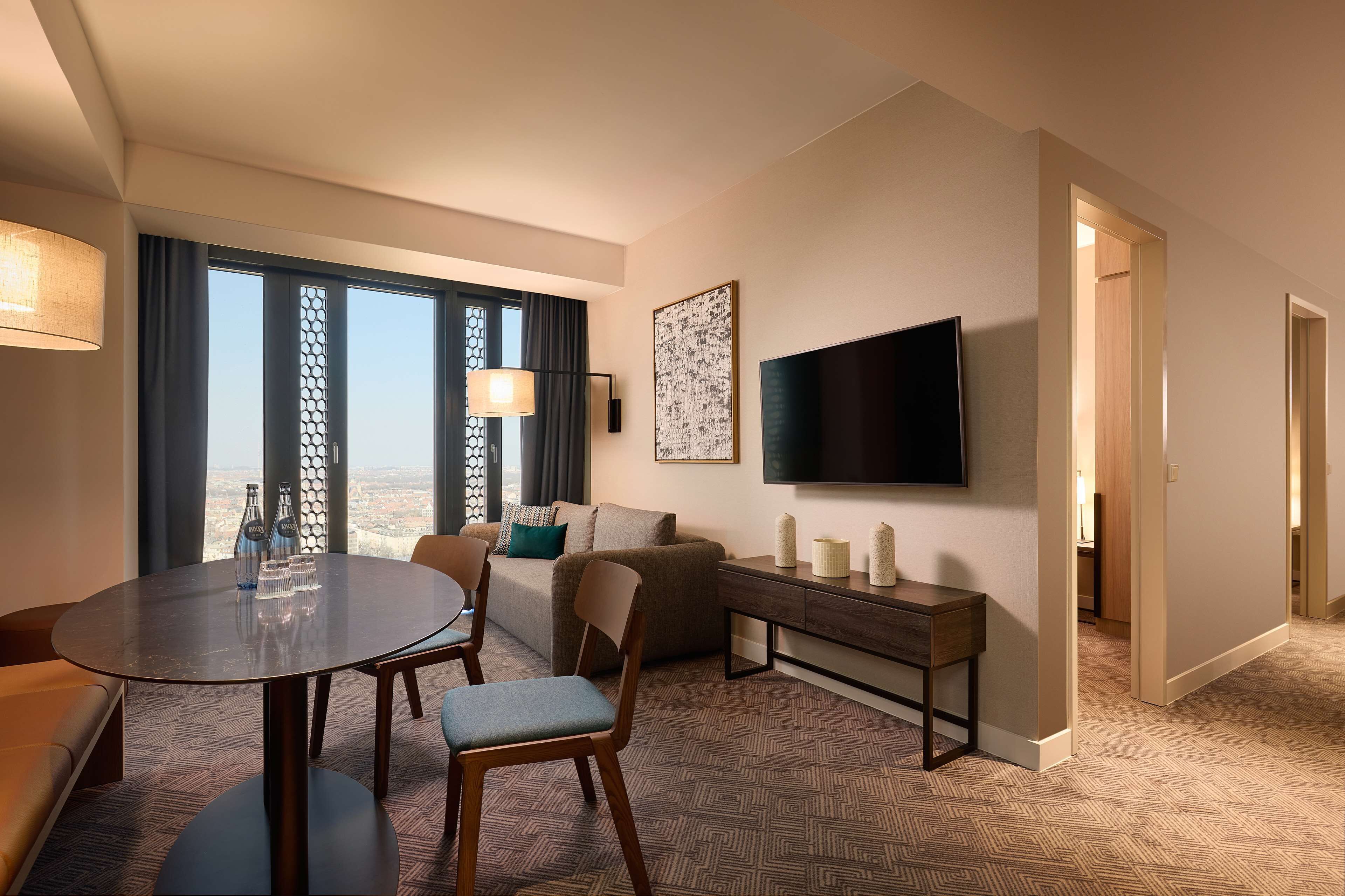 Habitación de hotel con comedor, sofá, televisión y vista de la ciudad.