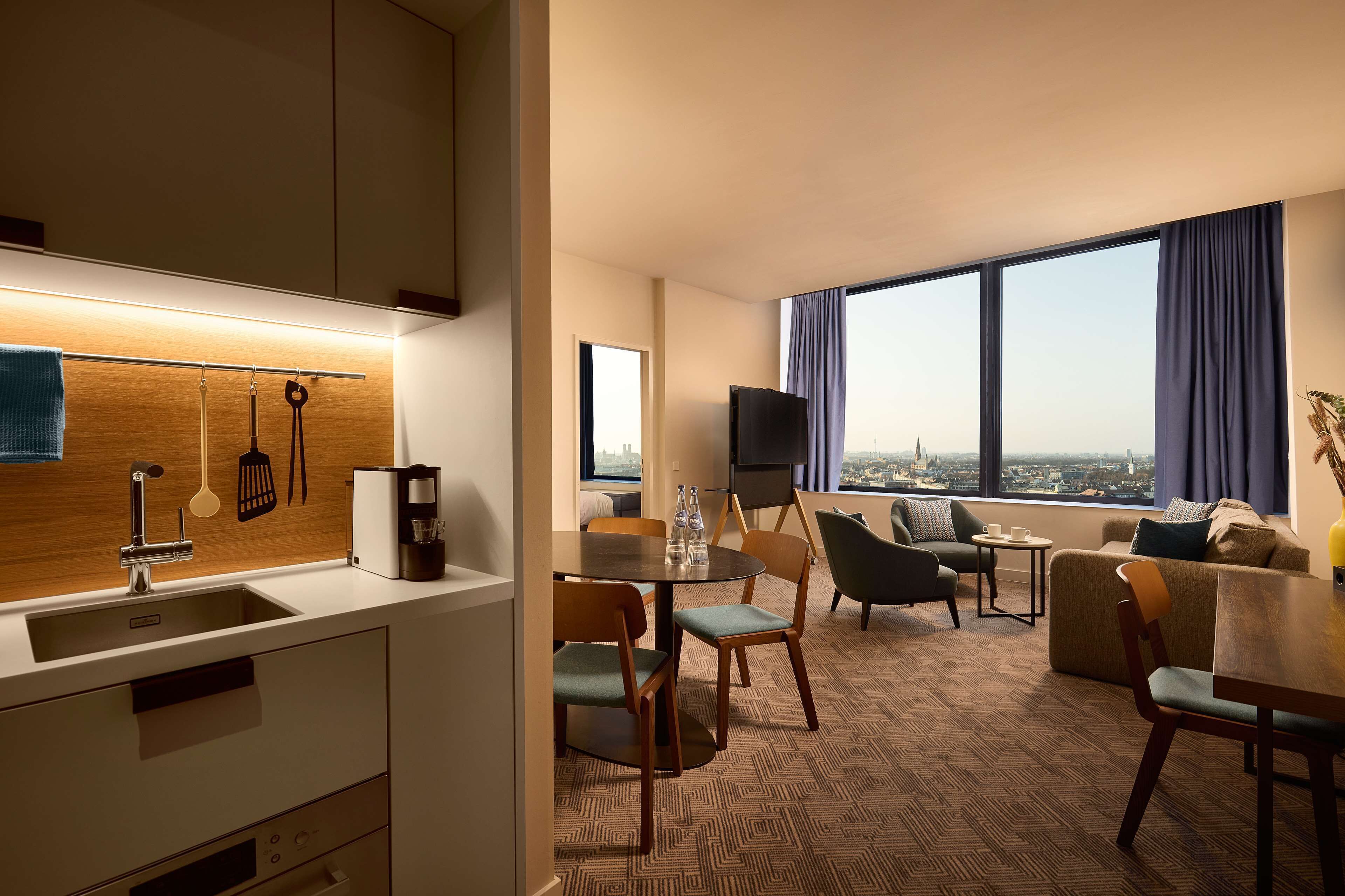 Une chambre d’hôtel moderne dotée d’un coin cuisine, d’un espace repas et d’un salon avec vue sur la ville.